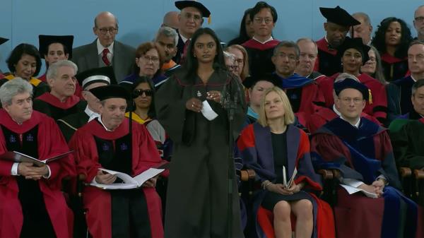 Kumar wears a dark-colored gown and holds a piece of paper while approaching the podium