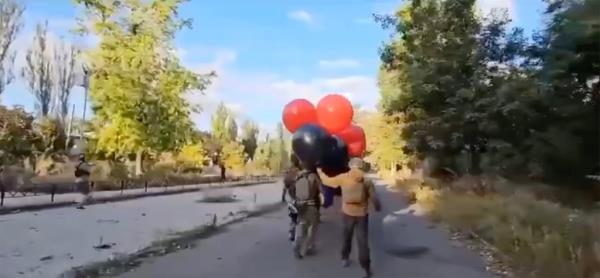 Soldiers in the Ukranian city of Avdiivka work to launch red and black helium balloons that will carry a flag skyward.
