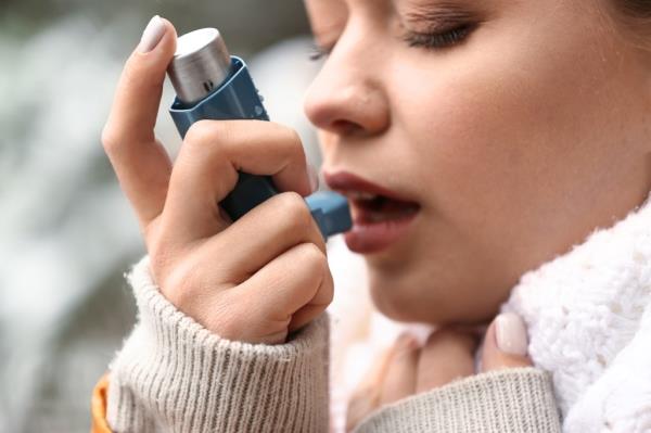Young woman using an inhaler outdoors