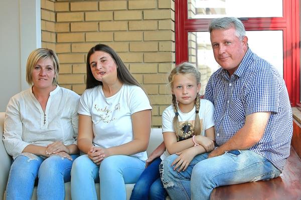 Family wearing blue denim jeans; blo<em></em>nde haired woman, teenager with facial disfiguration, young blo<em></em>nde girl, man in blue plaid shirt. 