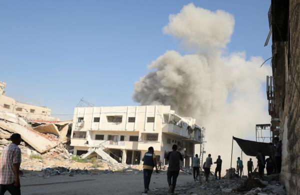 A group of people walking near a building in Gaza city with a large cloud of smoke rising following an Israeli strike on August 21, 2024.