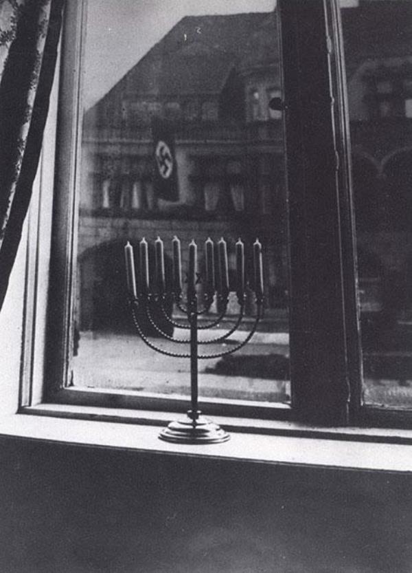 Lighted menorah in window, with Nazi flag flying on building across the street