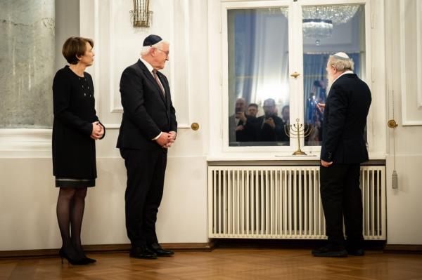 Yehuda Mansbach lighting a menorah, while German president Frank-Walter Steinmeier and First Lady Elke Büdenbender look on