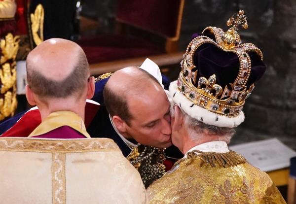 Prince William kissing his father, King Charles III, adorned with St Edward's Crown, during the Coro<em></em>nation Ceremony inside Westminster Abbey