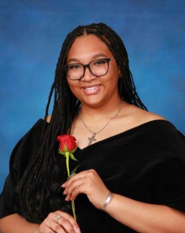 Young woman wearing glasses and holding a red rose receiving scholarship award from Yankees Pitcher Marcus Stroman at Yankee Stadium game.