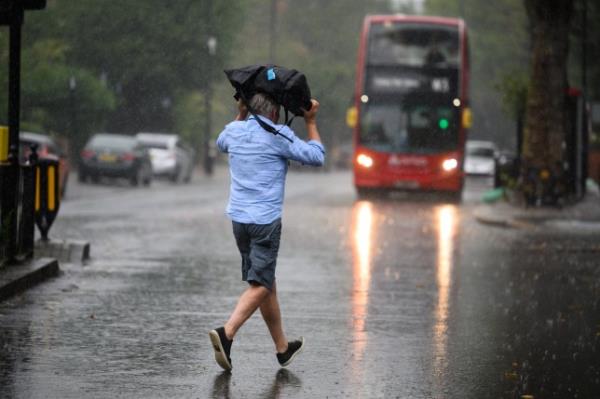 LONDON, ENGLAND - AUGUST 17: A man uses a bag for shelter as he crosses the road, as torrential rain and thunderstorms hit the country on August 17, 2022 in London, England. After the UK experienced a second summer heatwave, storms are expected starting in the north of the country from Mo<em></em>nday moving to the whole country by Wednesday, with flood a<em></em>lerts issued by the Met Office. (Photo by Leon Neal/Getty Images)