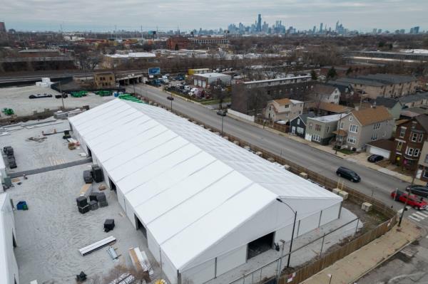 Government-run tent encmpment in Chicago aeriel view with city skyline in background.