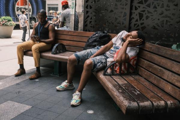 A man sleeps on a bench in a public plaza outside of a Holiday Inn on 8th avenue near 39th street in midtown Manhattan. 
