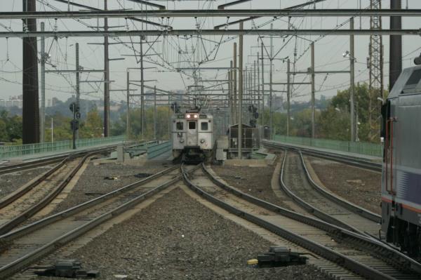 An NJ Transit train heads into the Frank R. Lautenberg Rail Station in Secaucus under catenary wires.