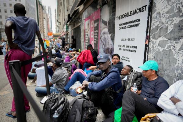 Migrants sit in a queue outside of The Roosevelt Hotel that is being used by the city as temporary housing