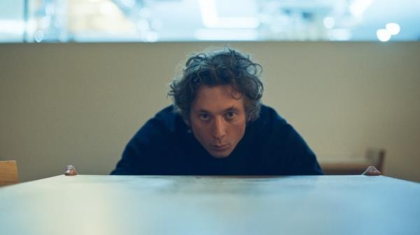 Jeremy Allen White bending over looking at something. 
