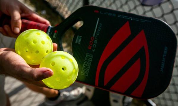 Closeup of pickleball paddle and hand holding two balls. 