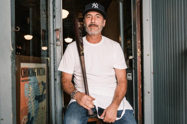 Mark Iacono, founder and owner of Lucali, sitting in a chair and holding a ba<em></em>seball bat gifted by New York Yankee Anthony Volpe.