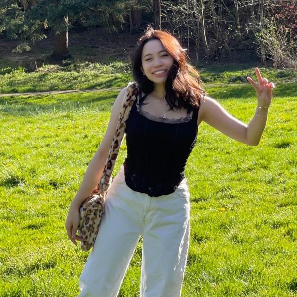 Angelina Tran is pictured in a black tank top and white pants giving a peace sign