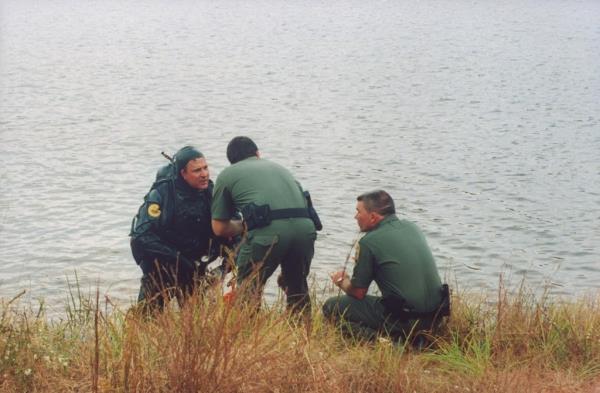 law enforcement officials, 1 clad in scuba gear, talking lakeside as they comb the water's bottom for the car of Susan Smith
