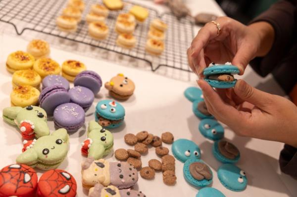stephanie tran holding  coo<em></em>kie mo<em></em>nster coo<em></em>kie, with different character coo<em></em>kies on table including spider-man, grogu and hello kitty