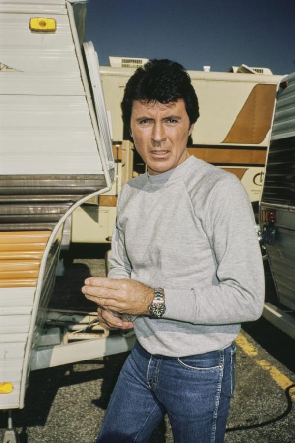 American actor and singer, James Darren, in a grey sweatshirt and jeans, standing next to trailers on a production backlot, circa 1983.