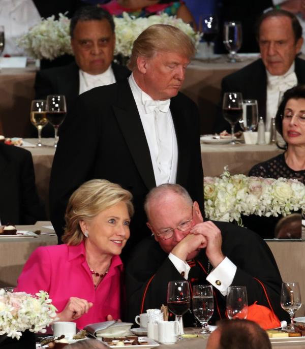 Do<em></em>nald Trump returning to his seat while Cardinal Timothy Dolan co<em></em>nverses with Hillary Clinton at the 71st annual Alfred E. Smith Memorial Foundation Dinner in New York