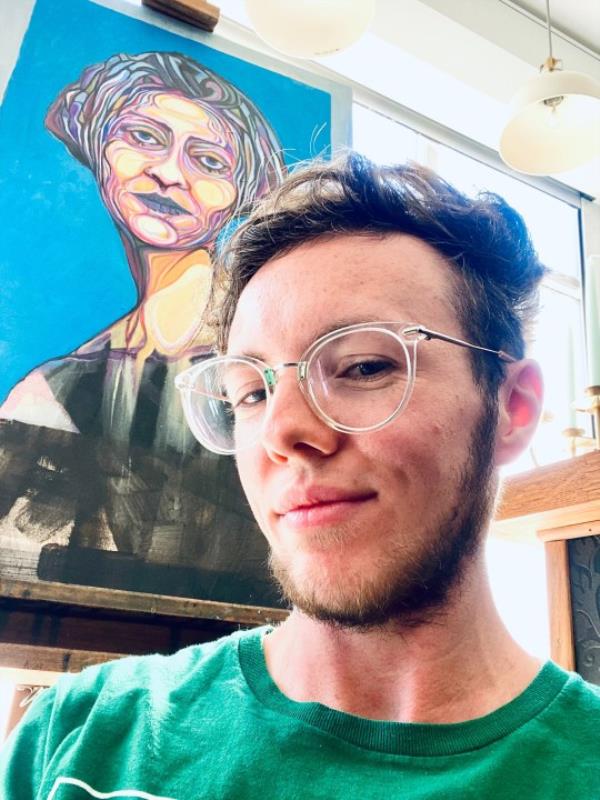 William Cuthbert taking a selfie before getting his tattoo, in a green t-shirt and glasses
