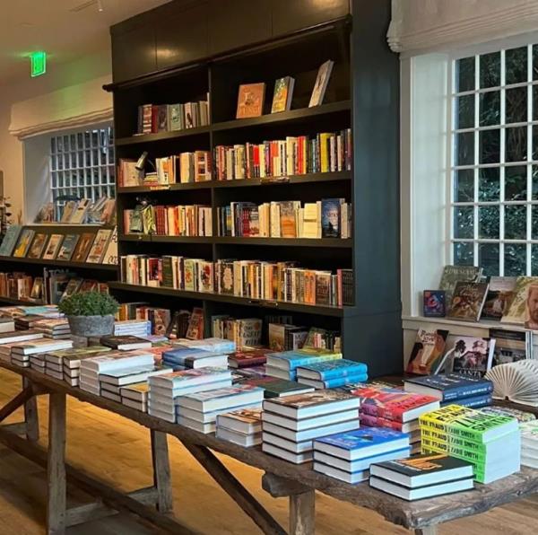 Meghan Markle and Oprah Winfrey at a local bookstore in California, with a display shelf featuring 'Spare' by the Duke of Sussex in the background.