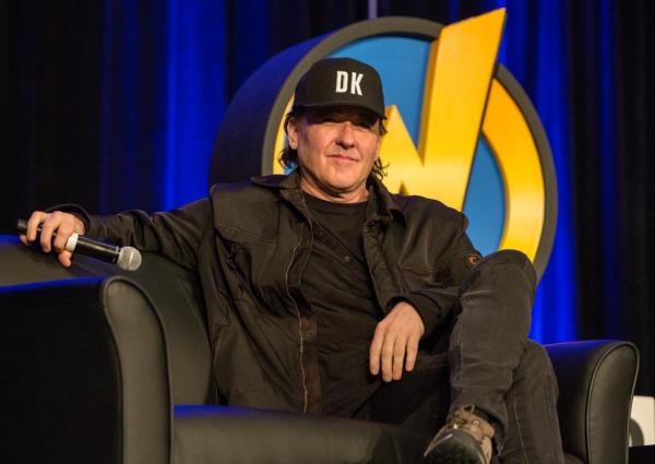 John Cusack sits on a chair. 
