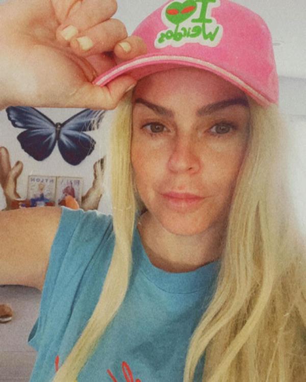 Taryn Manning looking at the camera with blo<em></em>nde hair and a pink hat. 