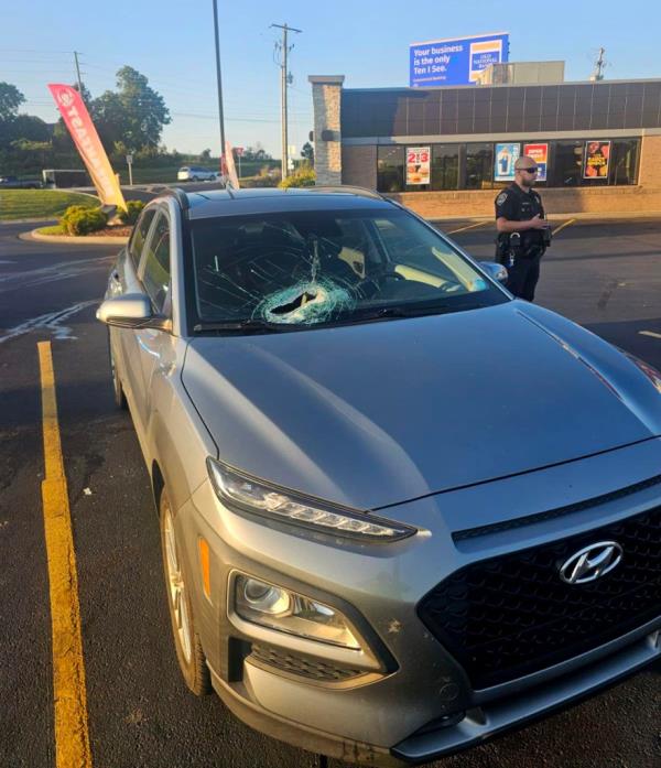 A gray Hyundai car with a smashed windshield following a tragic accident seen in fast food parking lot. Police officer seen in background.