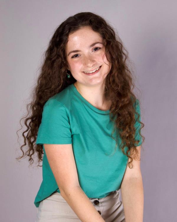 Autumn McClure, seen with long curly hair wearing a teal shirt and tan pants, posing for a photo in a photography lesson in college.