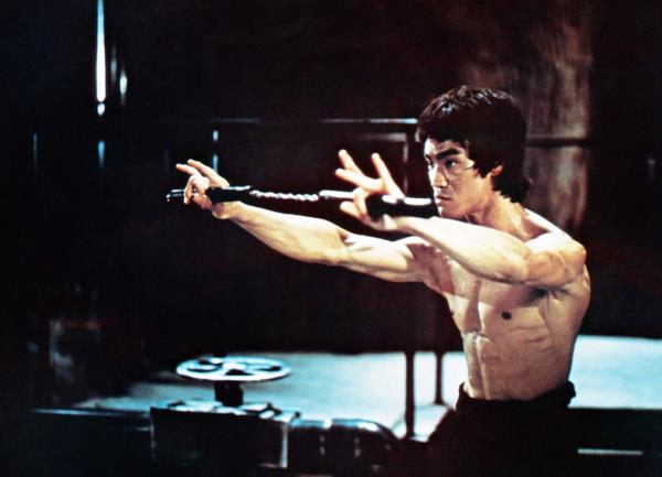 A photo of Bruce Lee in action with the martial arts sticks.