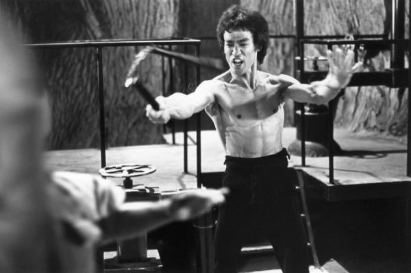 In the black and white  photo, Bruce Lee displays his martial arts skills using nunchaku in a scene from the 1973 film 