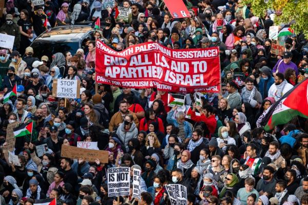 A large group of demo<em></em>nstrators waving Palestinian flags and holding anti-Israel signs, including a large red banner reading 