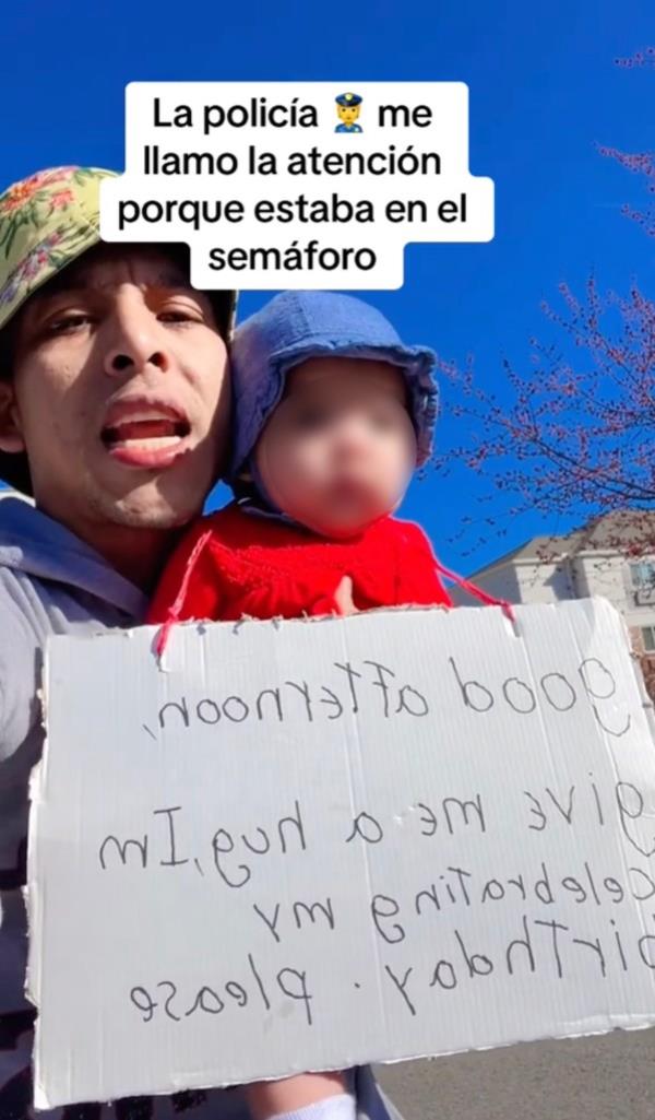 Migrant TikTokker holds up hand-scrawling sign. begging for cash with his daughter