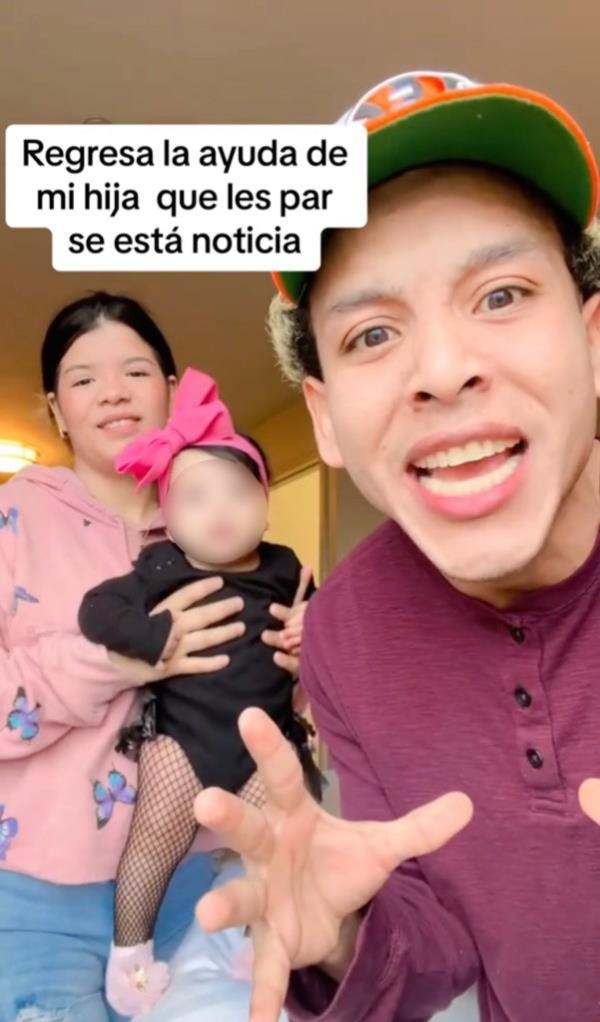 A woman holds a baby with a man in front.