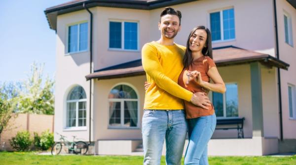 Excited young couple in love holding keys and hugging in front of their new modern house
