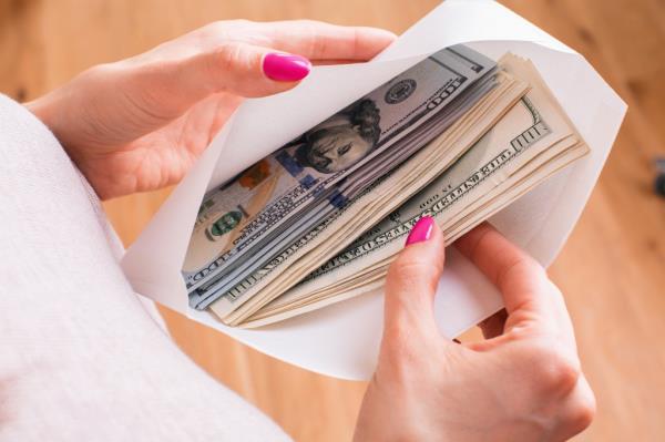 Woman's hands holding envelope full of dollar bills on a wooden surface, co<em></em>ncept of bribery and corruption