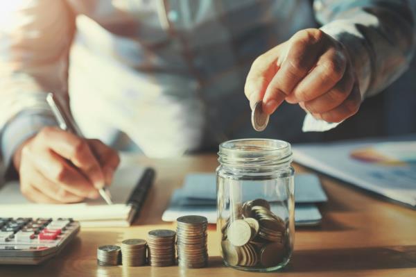 Businessman's hand placing coins into a glass jar for savings concept