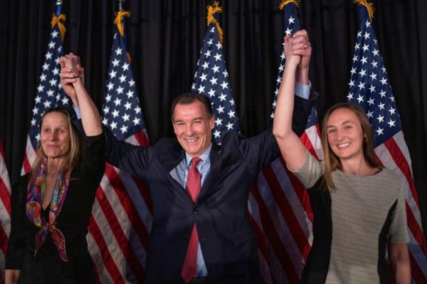 People holding hands in front of flags with Thomas Suozzi.