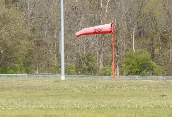 A red windsock on a pole at Clarksville Municipal Airport with a twin-engine prop plane that lost power during takeoff in the distance.