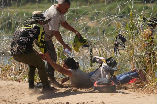 A migrant who crossed into the U.S. from Mexico is pulled under co<em></em>ncertina wire along the Rio Grande river, Thursday, Sept. 21, 2023, in Eagle Pass, Texas. 