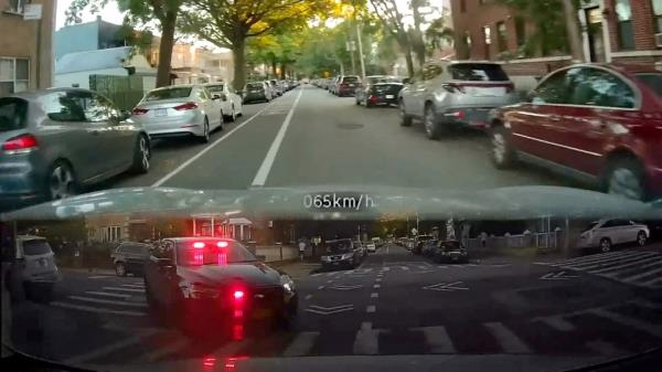 Screenshot of video of motorist driving on in Astoria with rearview recording of police car chasing them with lights flashing.