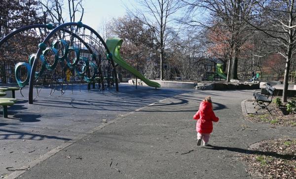 Toddler girl seen from behind in winter coat running through playground.