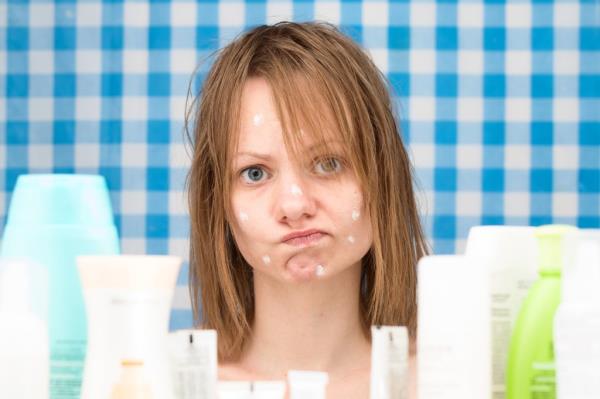 Young girl with wet hair and no makeup looking surprised at skincare products in bathroom