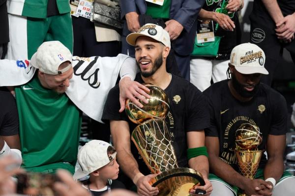 Jayson Tatum (c.) holds the Larry O'Brien Trophy alo<em></em>ngside Jaylen Brown (r.) and Kristaps Porzingis (l.) after the Celtics win the NBA champio<em></em>nship on June 17, 2024.