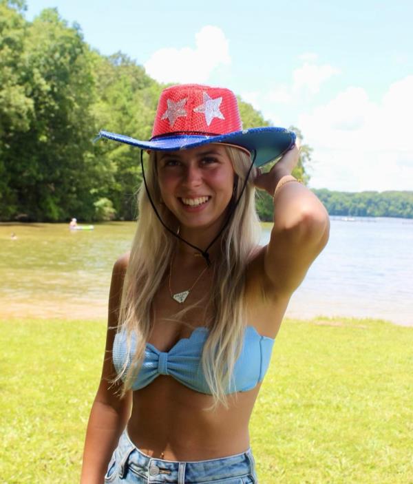 'Hawk Tuah Girl' Haliey Welch wearing red and blue sequined cowboy hat and bikini top in front of water