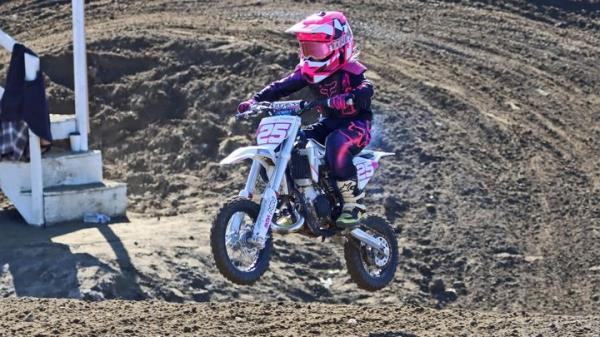 Brooke Carlton with helmet and gear on riding her motocross bike on a dirt track. 