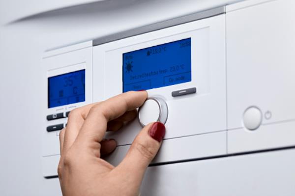 Cropped hand of woman adjusting knob on heating boiler's co<em></em>ntrol panel