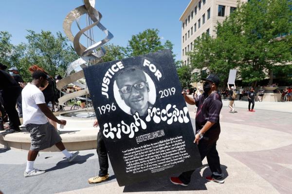 Demo<em></em>nstrators carrying a large placard with a picture of Elijah McClain wearing a black hat during a rally and march outside a police department.