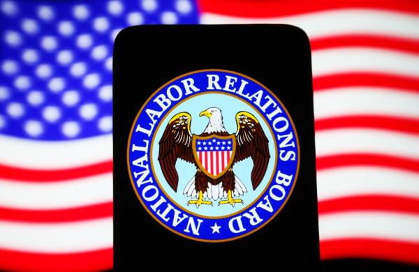 Natio<em></em>nal Labor Relations Board (NLRB) logo seen on a smartphone with the United States flag on a PC screen.