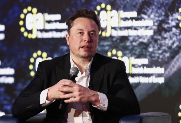 Elon Musk at a co<em></em>nference with a microphone, dressed in a suit.